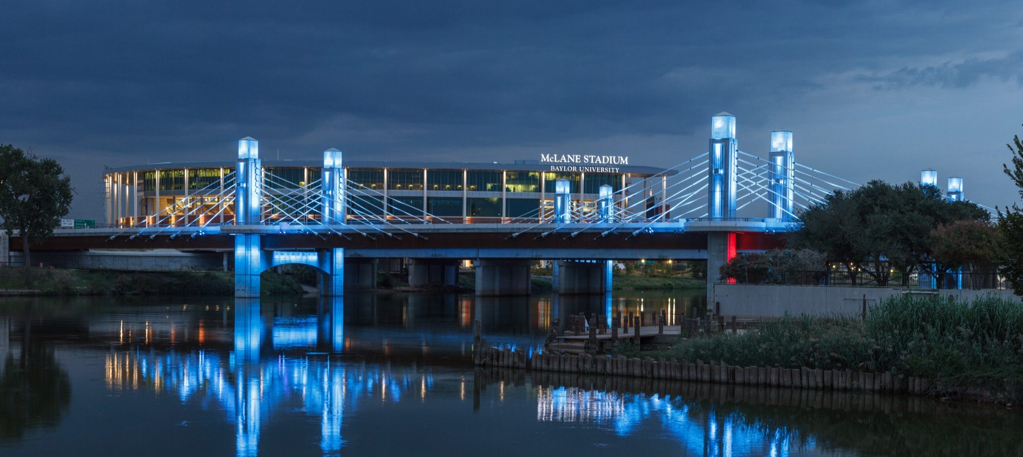 The pedestrian bridge lit blue in front of McLane Stadium in Waco at dusk